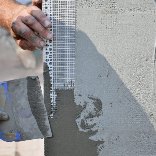 Hands of an old manual worker with wall plastering tools renovating house. Plasterer renovating outdoor walls and corners with spatula and plaster. Wall insulation. Construction finishing works